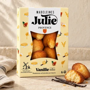 Boîte de 6 madeleines Julie à la vanille de Madagascar, blason provençal et moulin, avec des madeleines sur une table en pierre claire.